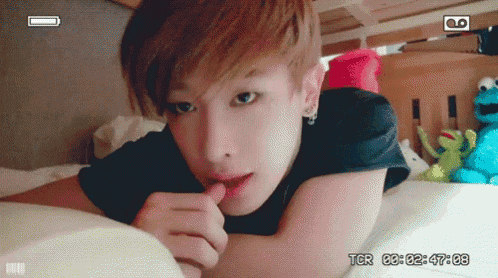 a young man is laying on a bed with a sesame street stuffed animal in the background .