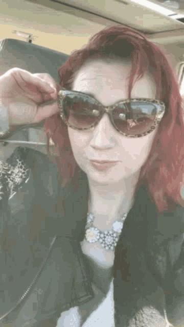 a woman with red hair wearing sunglasses and a black jacket
