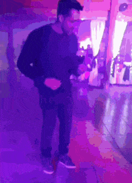 a man is dancing in a dark room with purple lights behind him