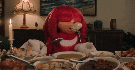 a red stuffed animal is sitting at a table with a spoon in its mouth