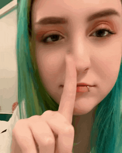 a woman with green hair is holding her finger to her lips