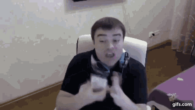 a man wearing headphones is sitting in a chair holding a cell phone and making a funny face .