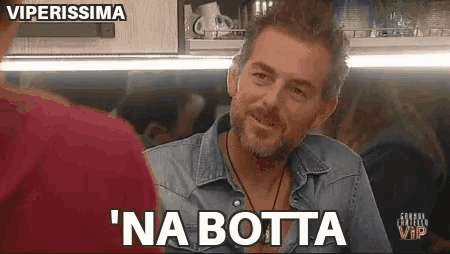 a man with a beard is sitting at a table with a woman and says na botta .