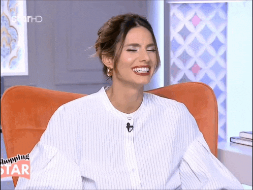 a woman is laughing while sitting in an orange chair with a shopping star logo in the background