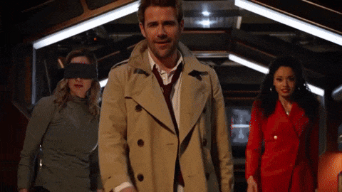 a man in a trench coat stands between two women with blindfolds on their eyes