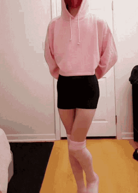 a woman wearing a pink hoodie and black shorts