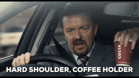 a man in a suit and tie is driving a car while holding a costa coffee cup