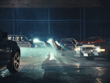 a group of women are dancing in a parking lot with cars in the background
