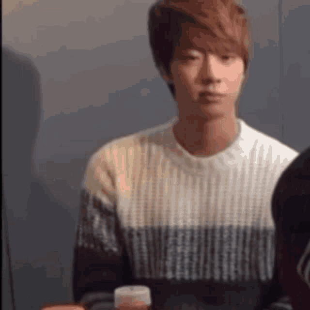 a man in a sweater is sitting at a table with a bottle of soda .