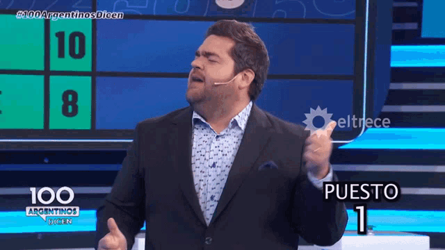 a man in a suit stands in front of a board that says puesto 1