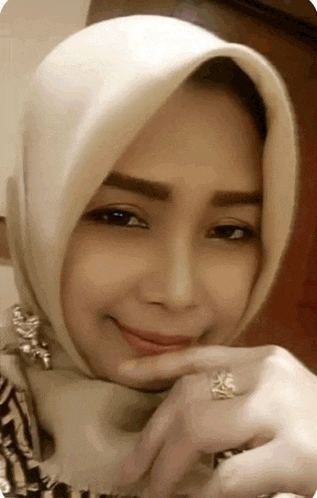 a woman wearing a hijab and a ring on her finger is smiling