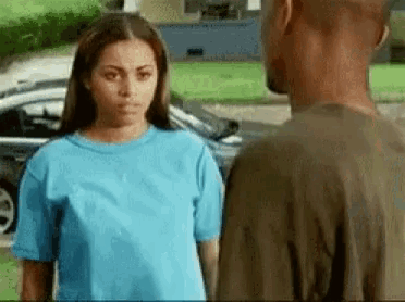 a man and a woman are standing next to each other in front of a car . the woman is wearing a blue shirt .