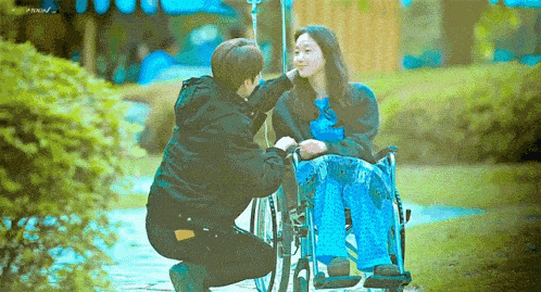 a man is kneeling down in front of a woman in a wheelchair .