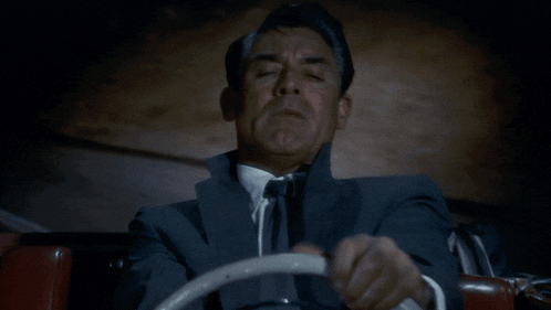 a man in a suit and tie is driving a red car