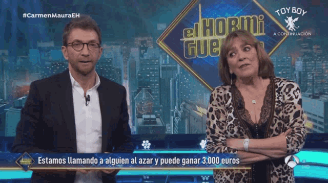 a man and a woman are standing in front of a screen that says el hormi gue