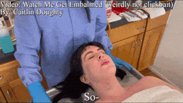 a woman is laying on a table with the words watch me get embalmed below her