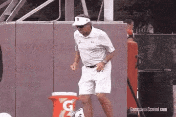 a man in a white shirt and white shorts is dancing in front of a gatorade cooler .