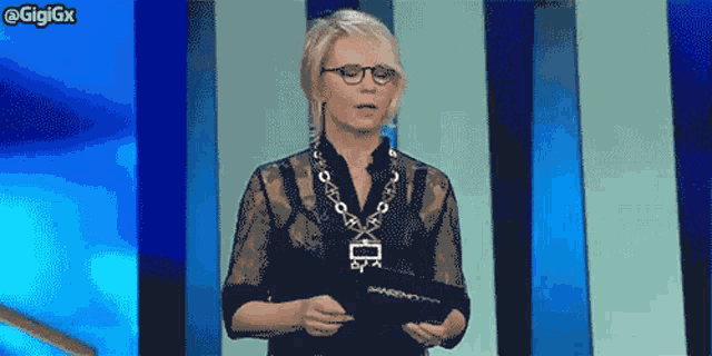 a woman wearing glasses and a necklace holds a clipboard with the word gigigx on the bottom right