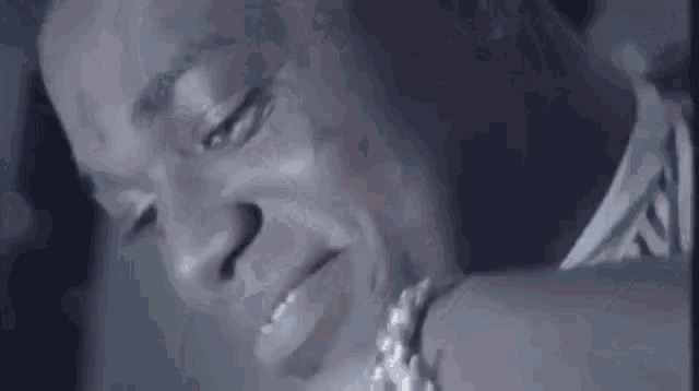 a close up of a man 's face with his eyes closed and a necklace around his neck .