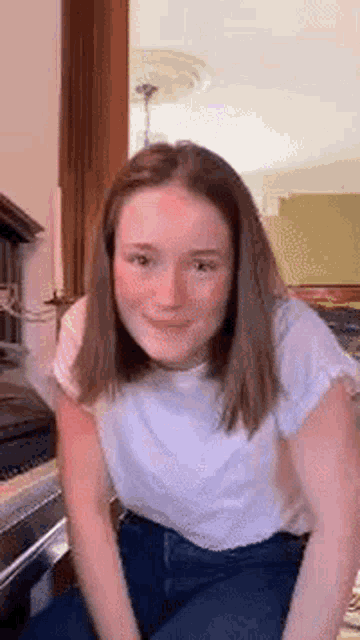 a young woman in a white shirt and blue jeans is smiling while sitting on a couch .