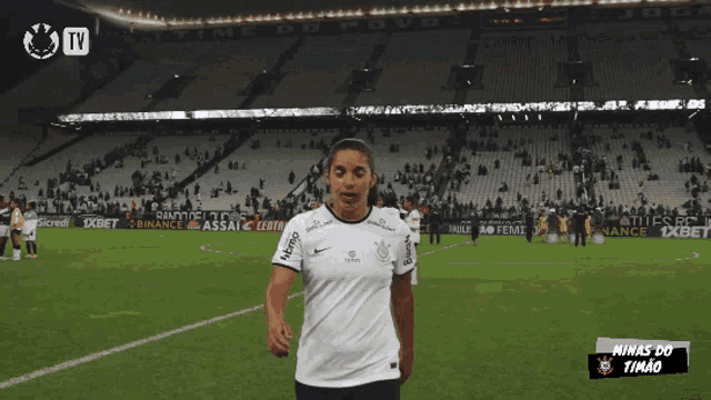 a woman stands on a soccer field with minas do timão on the bottom