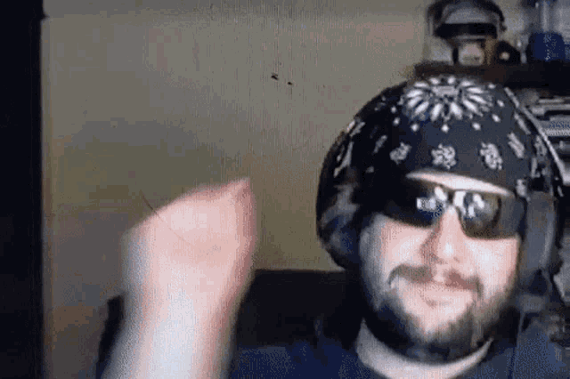 a man with a beard wearing a bandana and sunglasses is making a fist .