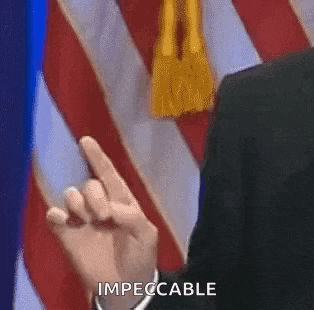 a man in a suit and tie is giving a finger in front of an american flag and says impeccable .
