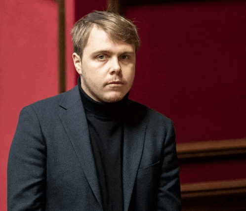 a man wearing a black turtleneck and a suit looks at the camera