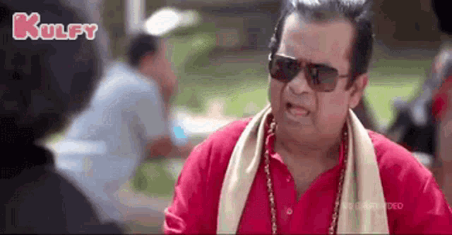 a man in a red shirt and sunglasses is talking to another man .