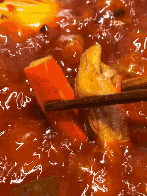 a close up of a person holding a piece of meat in a pot of sauce