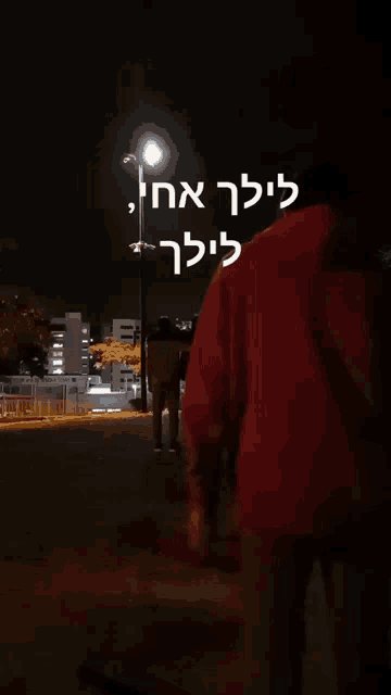 a group of people standing in a park at night with a sign in hebrew