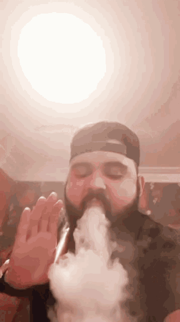 a man with a beard is smoking a hookah and blowing smoke out of his mouth