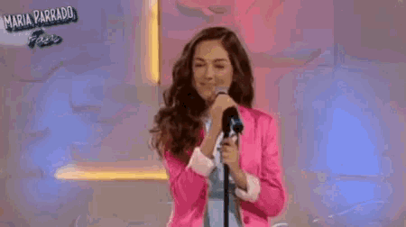 a woman in a pink jacket is singing into a microphone on stage .
