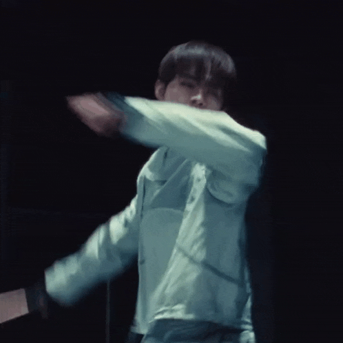 a man in a white jacket is dancing in a dark room with his arms outstretched .