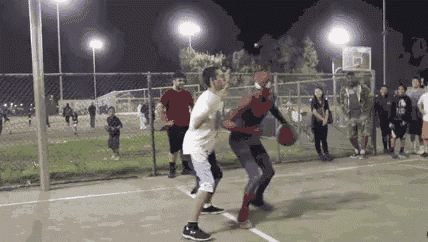 a man in a spiderman costume is playing basketball with a group of people .