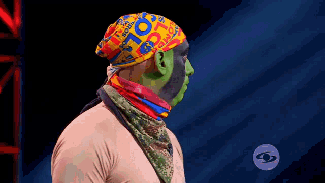 a man with green paint on his face wears a colorful headband that says ' colombia ' on it