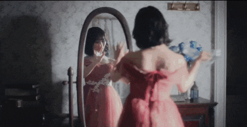 a woman in a red dress is standing in front of a mirror looking at herself .