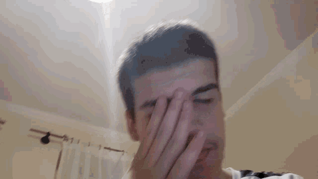a young man is covering his face with his hand while looking at the camera .