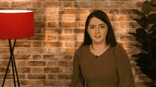 a woman standing in front of a brick wall with a red lamp in the background
