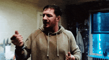 a man in a hoodie is standing in a room pointing at the camera .