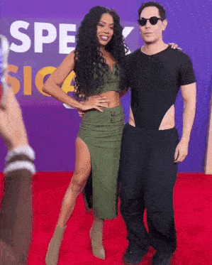 a man and a woman pose on a red carpet in front of a sign that says " spec "