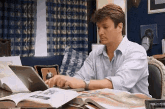 a man is sitting at a desk using a laptop and a book .