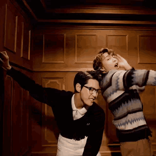 two men are standing next to each other in a room . one of the men is wearing glasses .