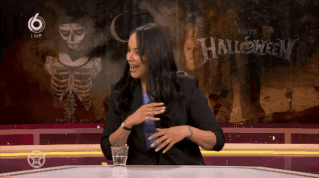 a woman sits at a table in front of a screen that says " happy halloween "