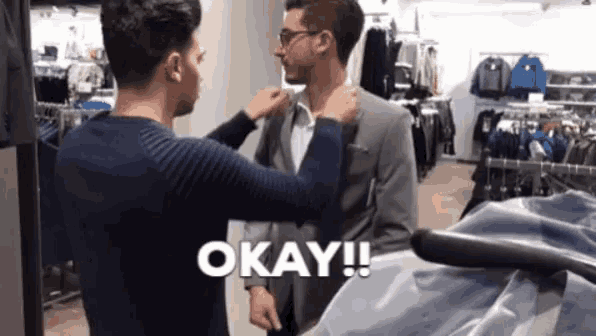 a man in a suit is being helped by another man and the words okay are visible