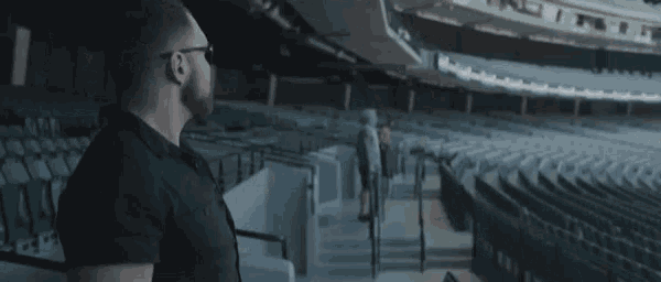 a man in a black shirt and glasses is standing in a stadium .