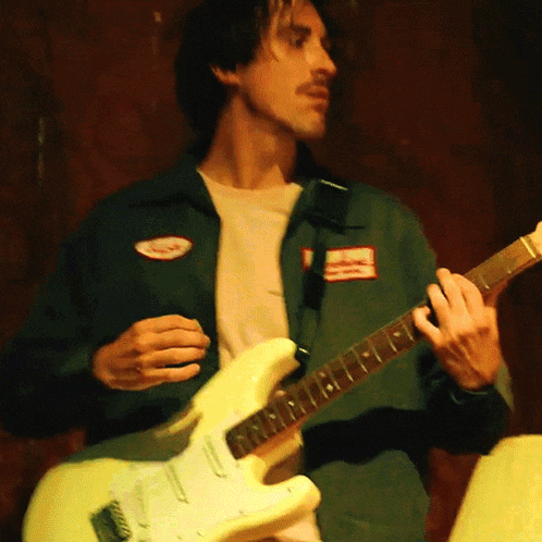 a man wearing a green jacket is playing a white guitar
