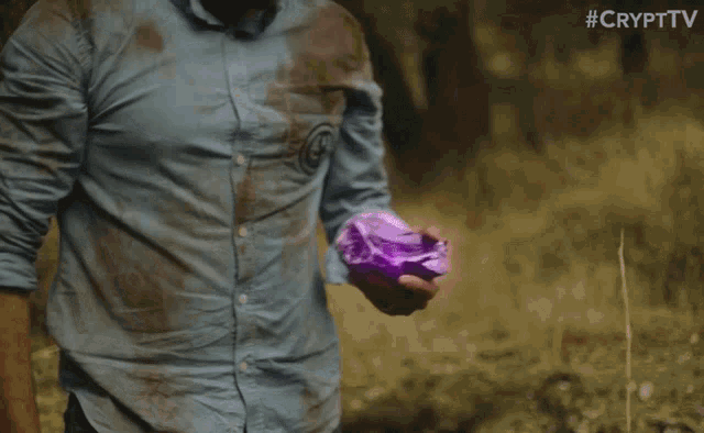 a man in a dirty shirt holds a purple object in his hand with #crypttv written on the bottom