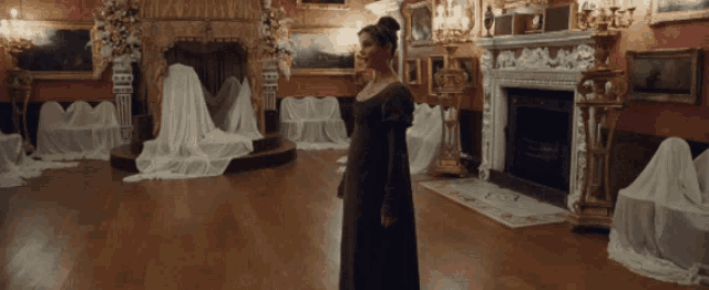 a woman in a black dress is standing in a room with a fireplace