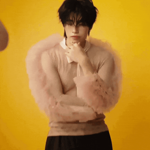 a man wearing a sweater with ruffled sleeves is standing in front of a yellow wall